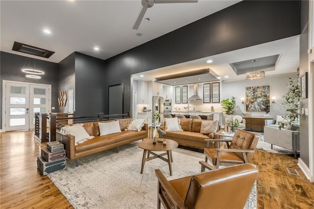 living room featuring a tray ceiling, light hardwood / wood-style floors, french doors, and ceiling fan