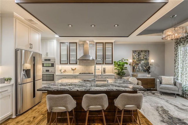 kitchen with stone counters, white cabinets, wall chimney exhaust hood, and appliances with stainless steel finishes