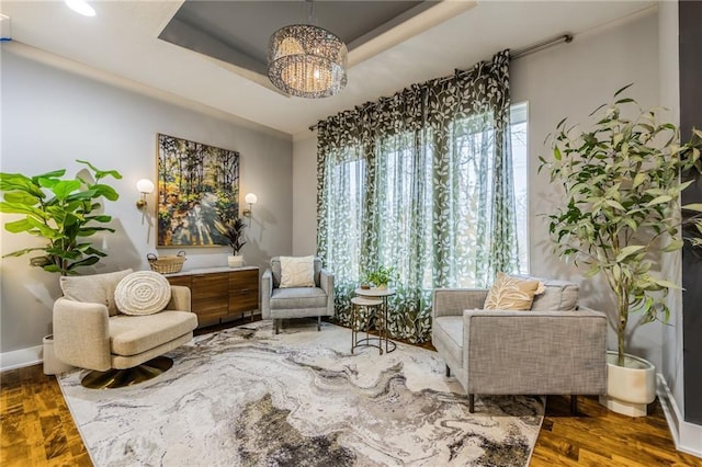 sitting room featuring a raised ceiling, hardwood / wood-style flooring, and a chandelier