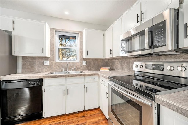 kitchen featuring stainless steel appliances, sink, white cabinetry, light wood-type flooring, and backsplash