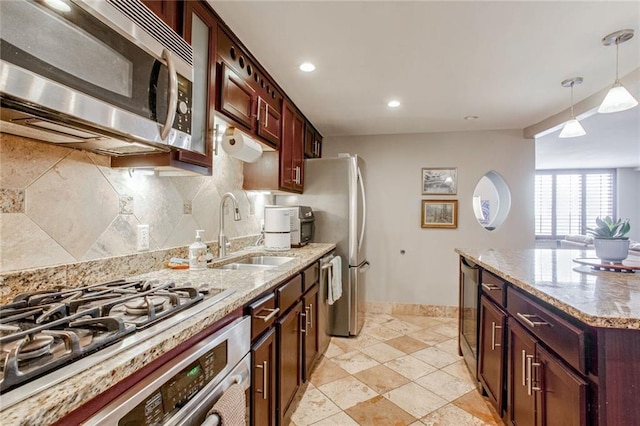 kitchen featuring sink, hanging light fixtures, decorative backsplash, appliances with stainless steel finishes, and light stone counters