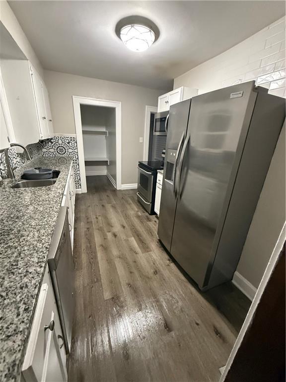 kitchen with appliances with stainless steel finishes, dark hardwood / wood-style flooring, light stone counters, sink, and white cabinetry