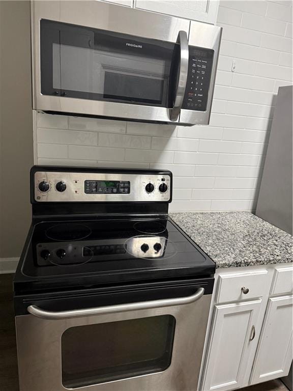 kitchen with light stone countertops, white cabinetry, appliances with stainless steel finishes, and backsplash