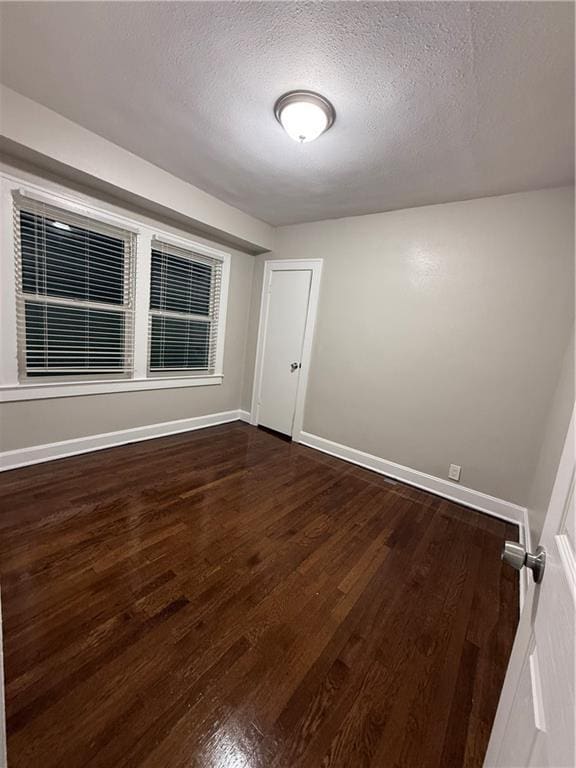 spare room featuring dark wood-type flooring, a textured ceiling, and baseboards