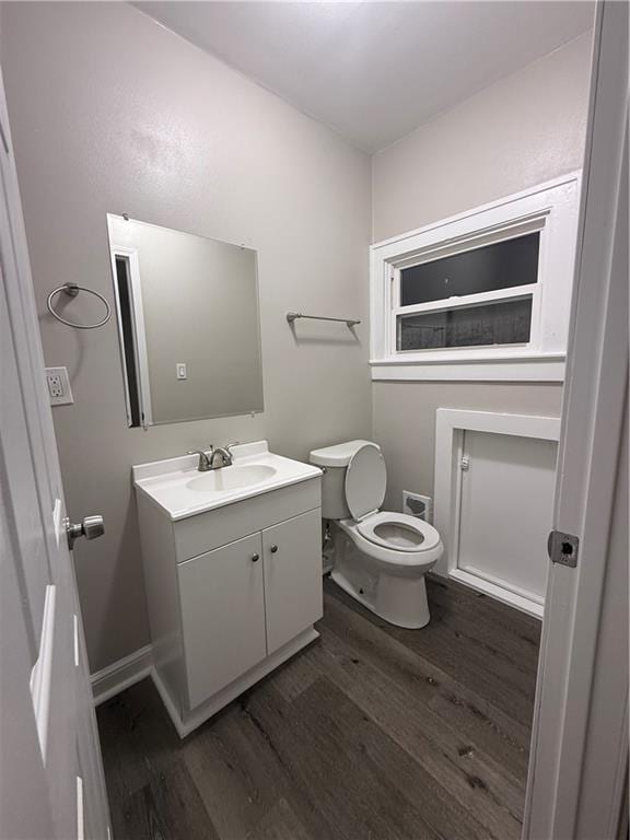 half bathroom featuring baseboards, vanity, toilet, and wood finished floors