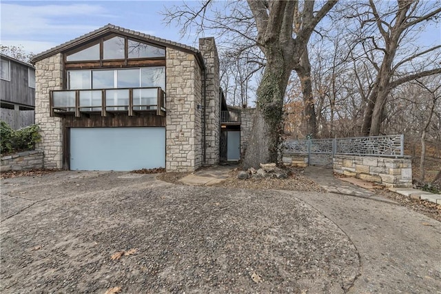 view of front of house featuring driveway, stone siding, fence, an attached garage, and a chimney