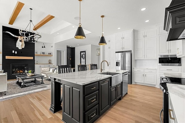 kitchen featuring appliances with stainless steel finishes, an island with sink, decorative backsplash, a large fireplace, and light hardwood / wood-style flooring