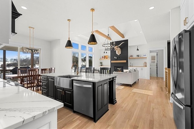 kitchen with decorative light fixtures, refrigerator, stainless steel dishwasher, a large fireplace, and light stone countertops