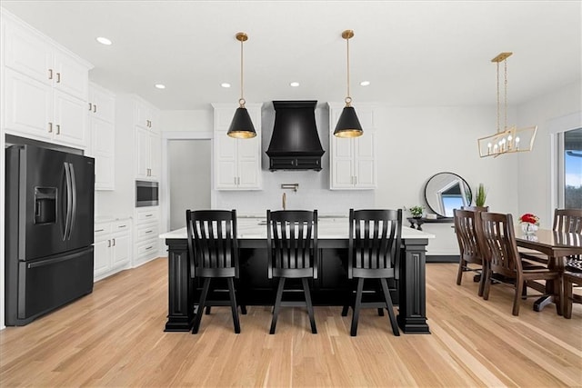 kitchen with a kitchen bar, black fridge, a kitchen island with sink, and custom exhaust hood