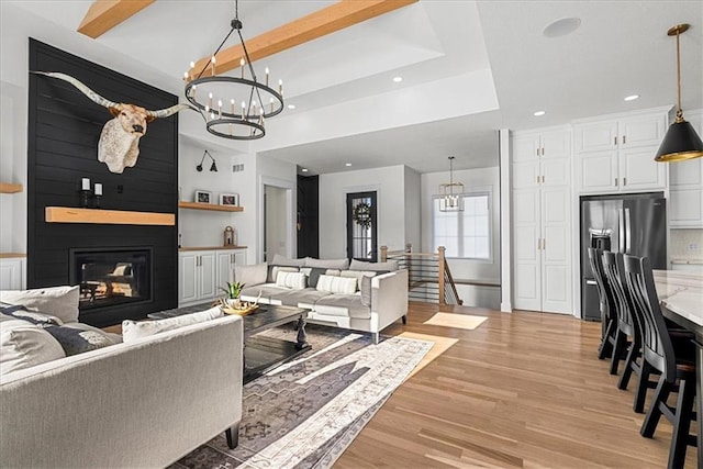 living room with a large fireplace, beamed ceiling, a chandelier, and light hardwood / wood-style flooring