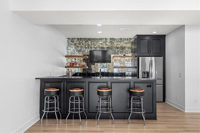 bar with sink, stainless steel fridge with ice dispenser, and light hardwood / wood-style floors