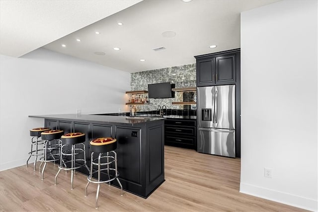 kitchen with a breakfast bar, stainless steel fridge, kitchen peninsula, and light wood-type flooring