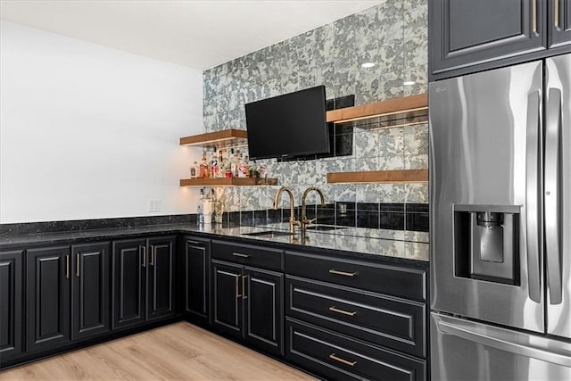 kitchen featuring light wood-type flooring, sink, stainless steel fridge with ice dispenser, and dark stone countertops