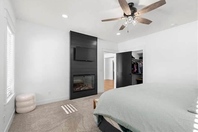 carpeted bedroom with ceiling fan, a large fireplace, a closet, and multiple windows