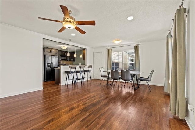 interior space featuring baseboards, decorative backsplash, dark wood-style floors, a breakfast bar area, and black appliances