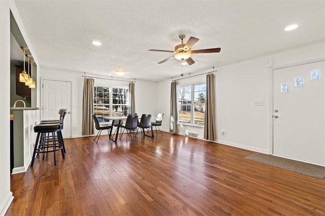 interior space with a textured ceiling, ceiling fan, wood finished floors, visible vents, and baseboards