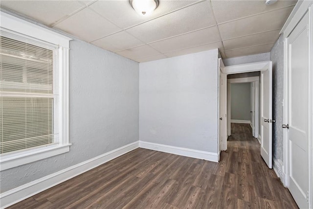 empty room with dark hardwood / wood-style flooring and a drop ceiling