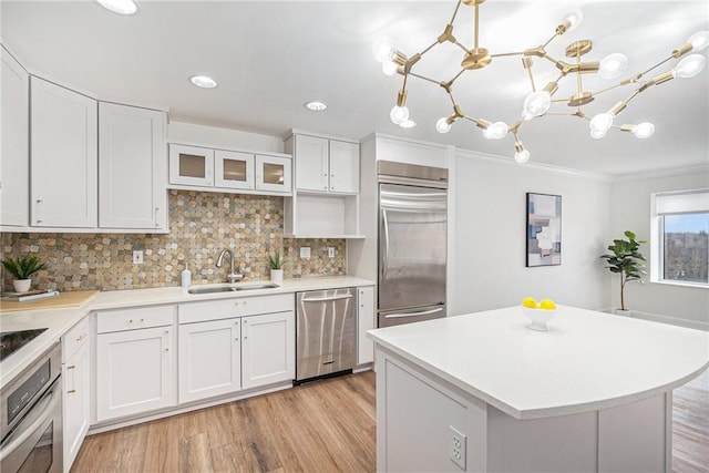 kitchen with sink, white cabinetry, hanging light fixtures, light hardwood / wood-style flooring, and stainless steel appliances