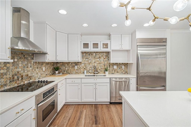 kitchen with white cabinets, stainless steel appliances, sink, and wall chimney range hood