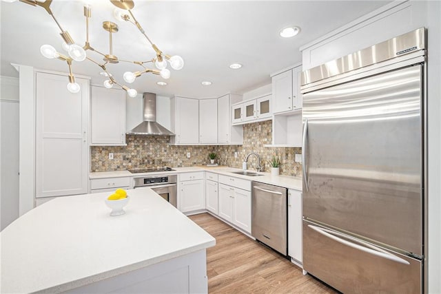 kitchen featuring wall chimney range hood, sink, appliances with stainless steel finishes, hanging light fixtures, and white cabinets