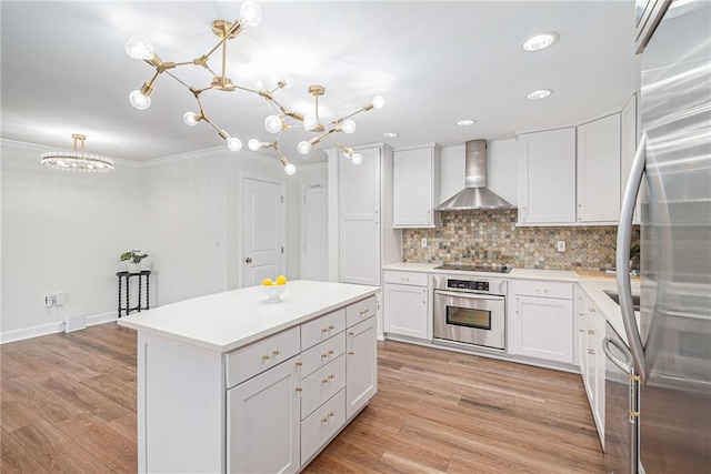 kitchen with wall chimney exhaust hood, white cabinetry, hanging light fixtures, a kitchen island, and stainless steel appliances