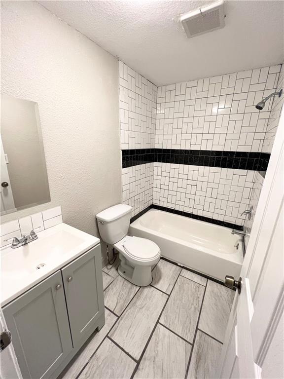 full bathroom featuring tiled shower / bath, vanity, toilet, and a textured ceiling