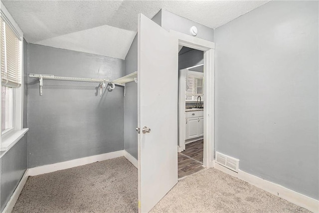 walk in closet with lofted ceiling, sink, and light colored carpet