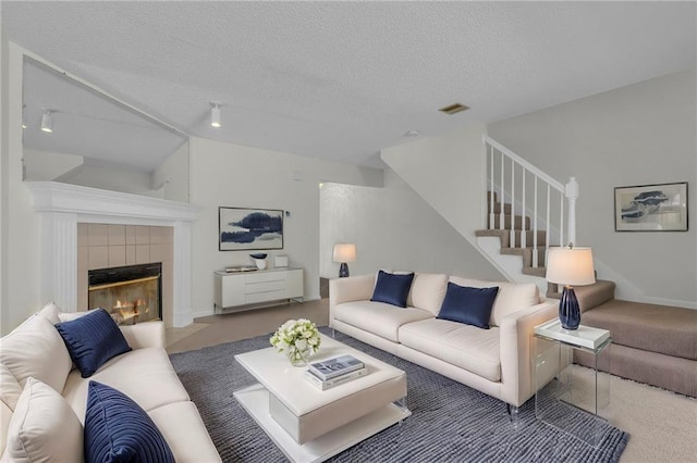 living room with a tile fireplace, lofted ceiling, carpet flooring, and a textured ceiling