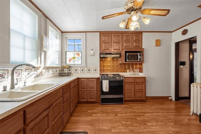 kitchen featuring sink, backsplash, light wood-type flooring, radiator, and stove