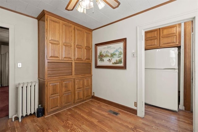 unfurnished dining area featuring wood-type flooring, radiator, ceiling fan, and crown molding