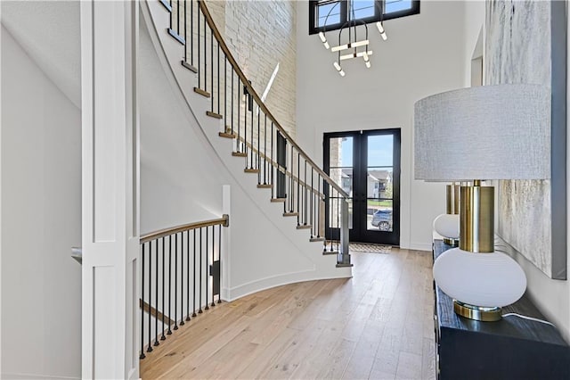 foyer entrance with wood finished floors, a towering ceiling, baseboards, stairs, and french doors