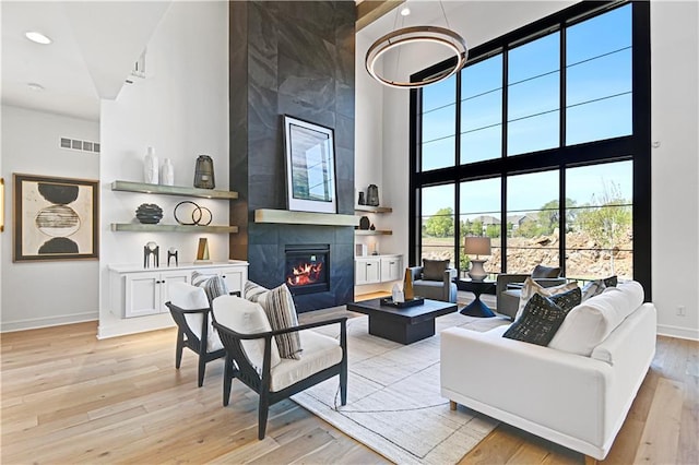 living room with baseboards, visible vents, a tiled fireplace, light wood-style flooring, and a high ceiling