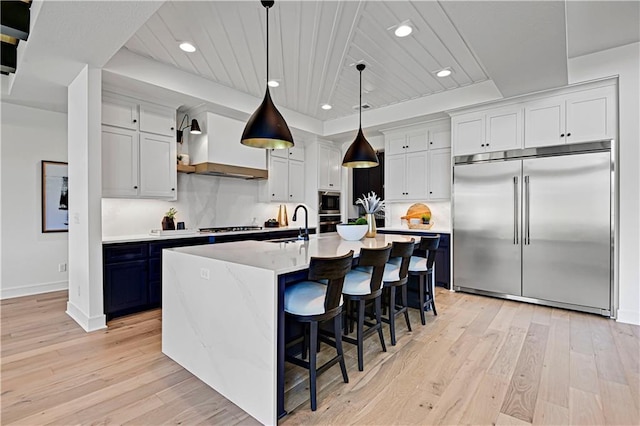 kitchen featuring built in appliances, a breakfast bar area, light wood-style floors, light countertops, and custom range hood