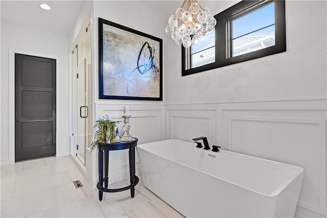 full bath featuring a freestanding tub, a decorative wall, wainscoting, a shower stall, and an inviting chandelier