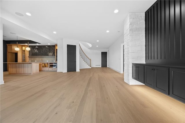 unfurnished living room with stairs, light wood finished floors, baseboards, and recessed lighting