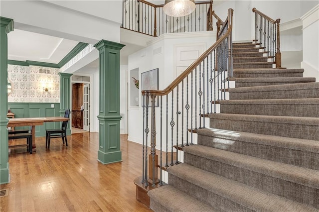 staircase featuring ornate columns, crown molding, and hardwood / wood-style flooring