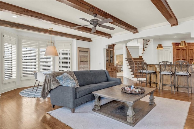 living room with beam ceiling, ceiling fan, and light wood-type flooring