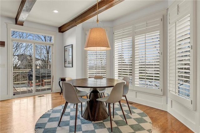 dining space with beam ceiling and light hardwood / wood-style floors