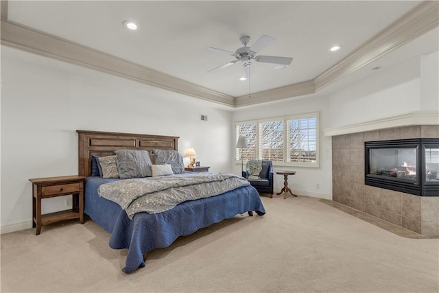 carpeted bedroom featuring crown molding, ceiling fan, a raised ceiling, and a tile fireplace