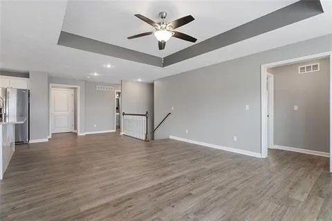 unfurnished living room featuring ceiling fan, dark wood-type flooring, and a raised ceiling