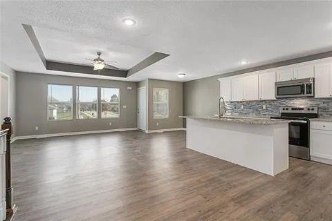 kitchen with appliances with stainless steel finishes, an island with sink, ceiling fan, a tray ceiling, and white cabinetry