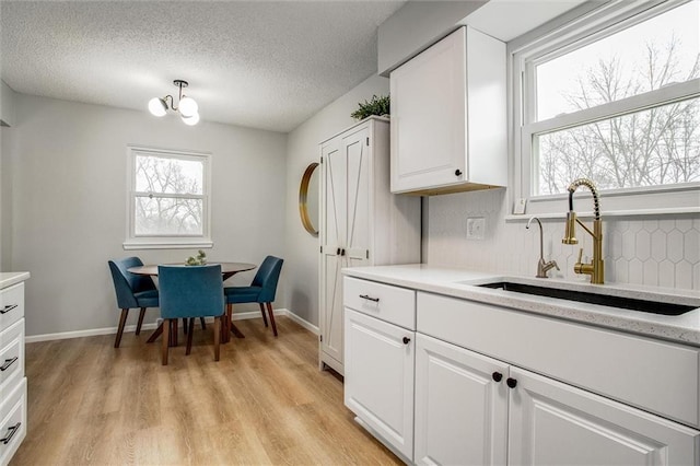 kitchen featuring sink, a textured ceiling, white cabinets, decorative backsplash, and light wood-type flooring