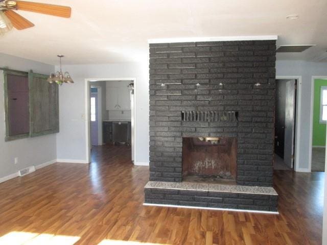 unfurnished living room featuring ceiling fan, wood finished floors, visible vents, baseboards, and a brick fireplace