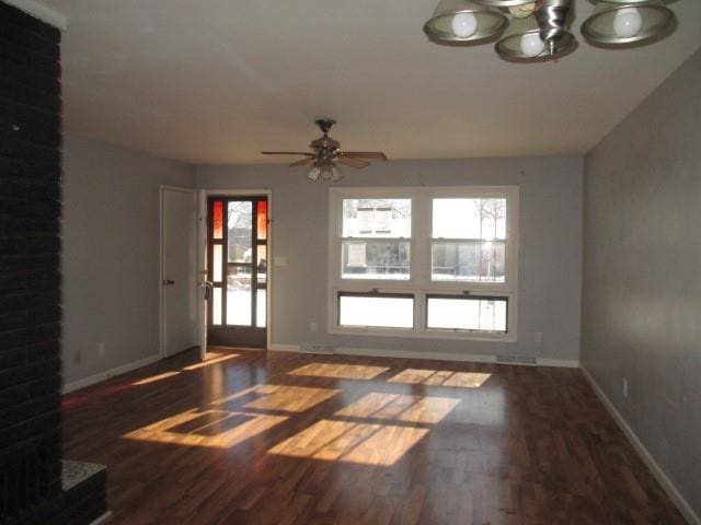 unfurnished living room with ceiling fan with notable chandelier, wood finished floors, and baseboards