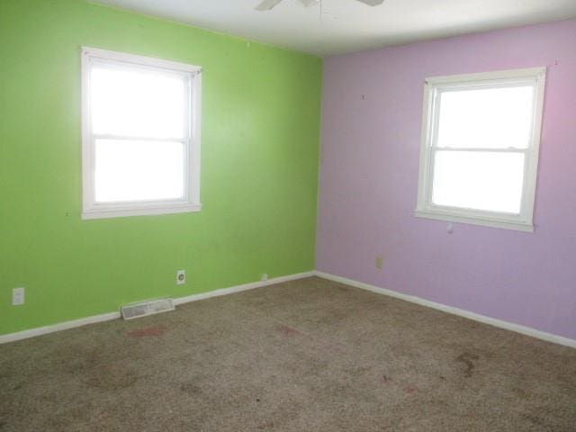 carpeted empty room featuring baseboards, visible vents, and a ceiling fan