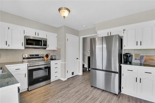 kitchen with backsplash, stainless steel appliances, light hardwood / wood-style flooring, and white cabinets