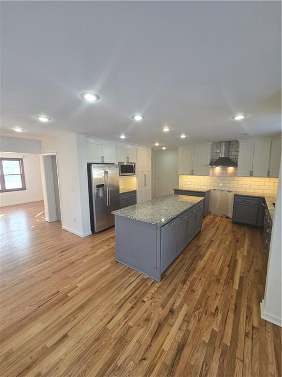 kitchen with light stone counters, light hardwood / wood-style flooring, a center island, stainless steel appliances, and wall chimney range hood