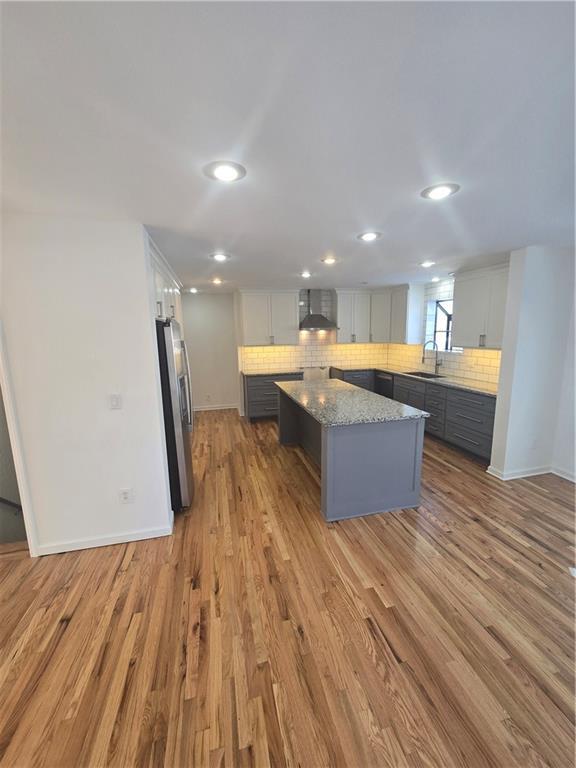 kitchen with a center island, stainless steel fridge, sink, white cabinetry, and wall chimney range hood