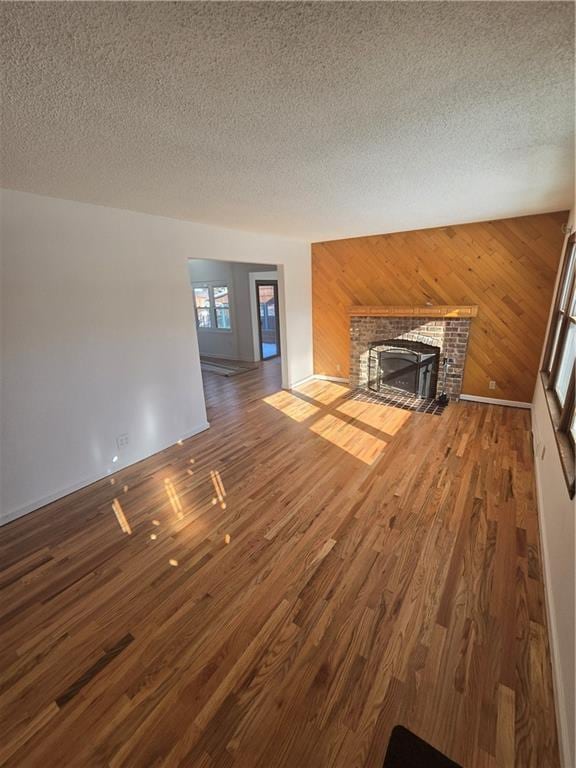 unfurnished living room featuring a brick fireplace, a textured ceiling, and wood walls