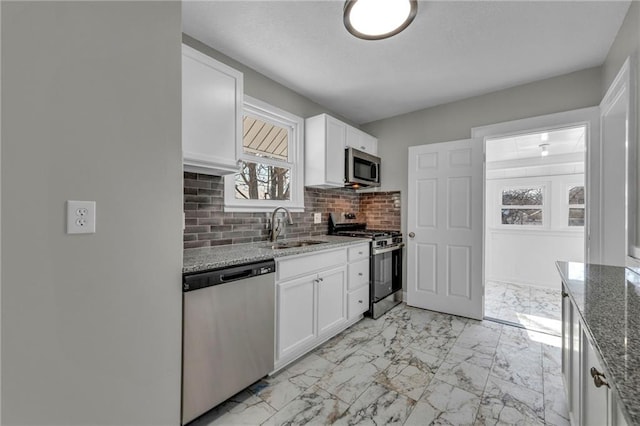 kitchen with light stone countertops, backsplash, white cabinets, appliances with stainless steel finishes, and sink